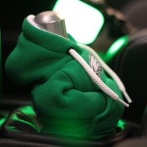May include: Green hooded sweatshirt with white drawstrings and a white eagle logo. The sweatshirt is sitting on a black surface.