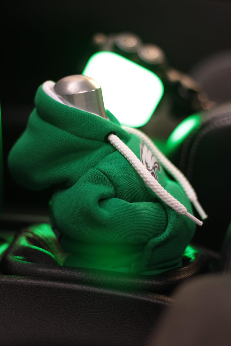 May include: Green hooded sweatshirt with white drawstrings and a white eagle logo. The sweatshirt is sitting on a black surface.