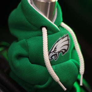 May include: Green and white hooded sweatshirt gear shifter cover with a white drawstring and an embroidered Philadelphia Eagles logo.