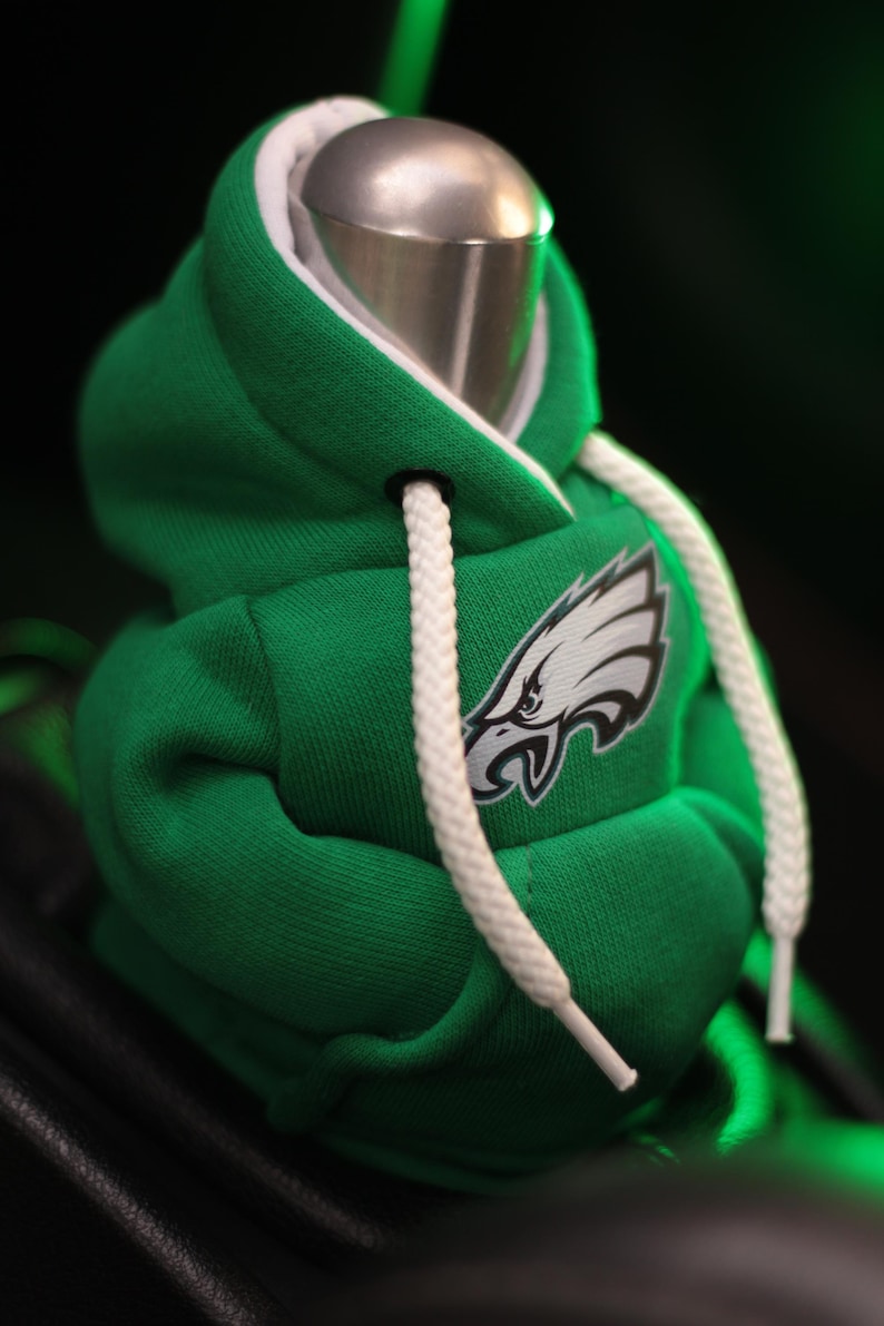 May include: Green and white hooded sweatshirt gear shifter cover with a white drawstring and an embroidered Philadelphia Eagles logo.