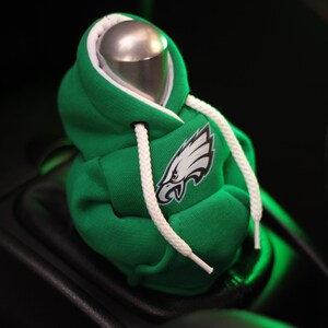 May include: Green and white hooded sweatshirt gear shift knob with a white eagle logo. The sweatshirt is made to look like a miniature hoodie.