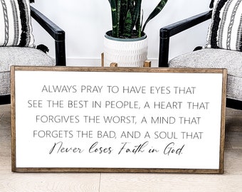 May include: A rectangular wooden sign with a white background and a dark brown frame. The sign features black text that reads: ALWAYS PRAY TO HAVE EYES THAT SEE THE BEST IN PEOPLE, A HEART THAT FORGIVES THE WORST, A MIND THAT FORGETS THE BAD, AND A SOUL THAT Never loses Faith in God.