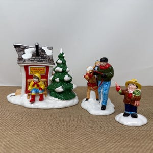 May include: A ceramic Christmas village scene featuring a red and white building with a sign that reads "Pony Rides", a green Christmas tree, and figurines of people and a pony. The figurines are on a snowy base.