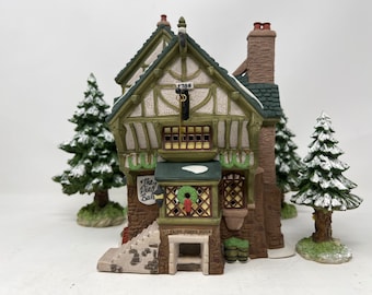 Puede incluir: Un edificio en miniatura detallado con una fachada verde y blanca, con un letrero que dice "The Pied Bull". El edificio tiene una chimenea, una corona y está rodeado de pinos en miniatura cubiertos de nieve. También es visible la dirección "33 Saint John's Moor".