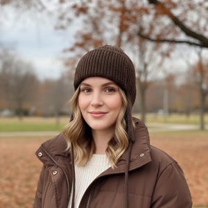 Könnte beinhalten: Eine braune Strickmütze mit Ohrenklappen. Die Mütze besteht aus geripptem Strickmaterial und ist ein warmes, gemütliches Accessoire. Die Mütze ist einfarbig und für kaltes Wetter geeignet.