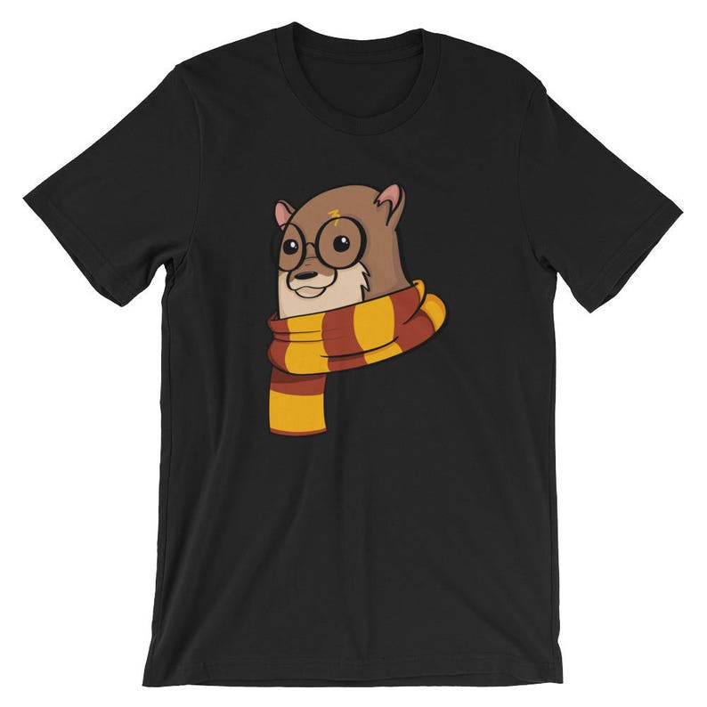May include: Black t-shirt featuring a cartoon otter wearing round glasses and a striped scarf in shades of gold and burgundy. The otter has a lightning bolt on its forehead. The design is centered on the front of the shirt.