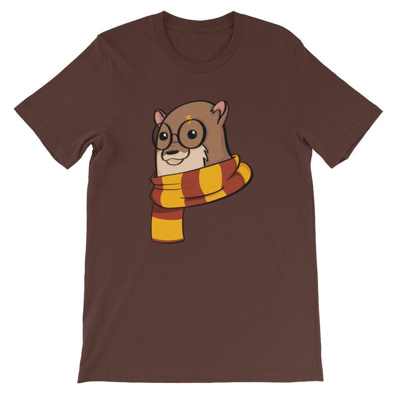 May include: A brown t-shirt featuring a cartoon otter wearing round glasses and a scarf with red and yellow stripes. The otter has a lightning bolt on its head. The shirt is a solid color.