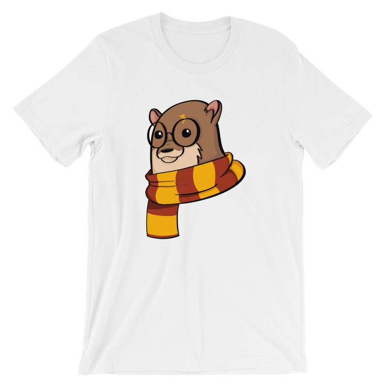 May include: White t-shirt featuring a cartoon otter wearing round glasses and a scarf with red and yellow stripes. The otter has a lightning bolt on its forehead. The shirt is made of a soft material.