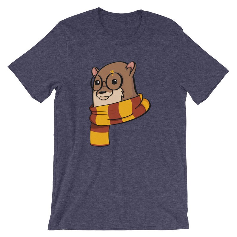 May include: Navy blue t-shirt featuring a cartoon otter wearing round glasses and a striped scarf in shades of yellow and burgundy. The otter has a lightning bolt on its forehead. The shirt is a short-sleeved crew neck.