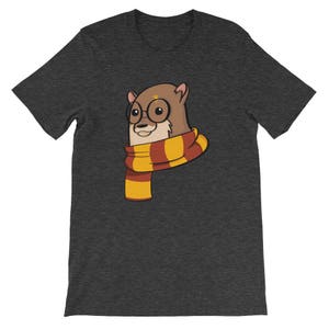 May include: Dark gray t-shirt featuring a cartoon otter wearing round glasses and a striped scarf in shades of yellow, orange, and red. The otter has a lightning bolt on its forehead. The shirt is a short-sleeved crew neck.