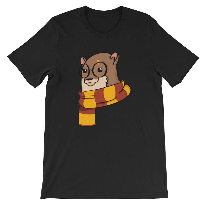 May include: Black t-shirt featuring a cartoon otter wearing round glasses and a striped scarf in shades of gold, red, and brown. The otter has a lightning bolt on its head. The design is centered on the front of the shirt.