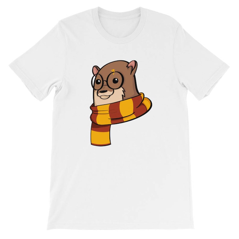 May include: White t-shirt featuring a cartoon otter wearing round glasses and a striped scarf in shades of red, yellow, and brown. The otter has a lightning bolt on its forehead. The shirt is a short-sleeved crew neck.