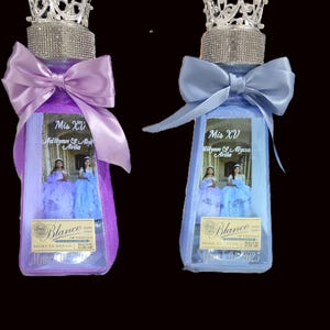 May include: Two decorated tequila bottles, one purple and one blue, for a quinceañera. Each bottle has a crown, bow, and a label with the text "Mis XV Adilynn & Alyssa Avila". The bottles are filled with glitter.