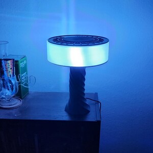 May include: A blue and black table lamp with a round, white shade and a twisted base. The lamp is on a dark wooden surface.