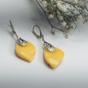 May include: A pair of dangle earrings featuring yellow amber stones and silver accents. The stones are teardrop shaped and have a smooth, polished finish.