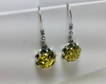 May include: A pair of dangle earrings featuring a silver hook and a cluster of olive-green, textured stones. The stones are encased in a decorative silver setting.