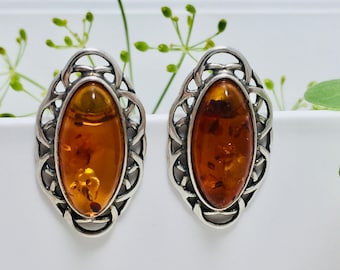 May include: A pair of silver earrings with amber oval stones set in a delicate, intricate design.