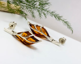 May include: A pair of silver earrings with amber leaf-shaped stones. The earrings have a delicate, intricate design.
