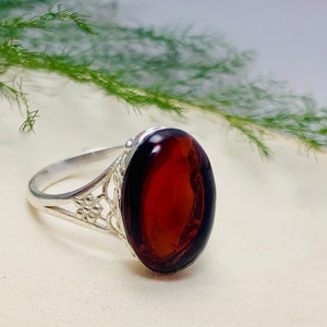 Pode incluir: Um anel de prata com uma gema oval de âmbar escuro engastada em um design filigranado.