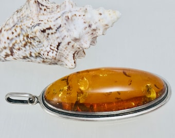 May include: A silver pendant with an oval amber stone. The amber is a warm honey color with flecks of gold throughout. The pendant is set in a silver bezel with a smooth, polished finish.
