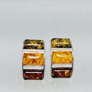 May include: A pair of silver hoop earrings featuring three rectangular amber stones. The stones are layered in shades of green, yellow, and brown.