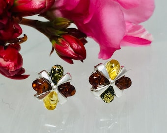 May include: A pair of silver earrings with a flower design. Each earring features five amber stones in shades of green, yellow, and brown.