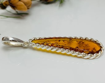 May include: A teardrop-shaped amber pendant with a silver rope-like border. The pendant is attached to a silver bail.