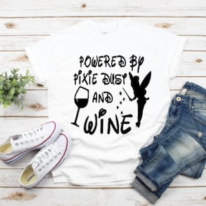 May include: White t-shirt with black text that reads "Powered by Pixie Dust and Wine". A silhouette of a fairy with a wand and a glass of wine are also included in the design.