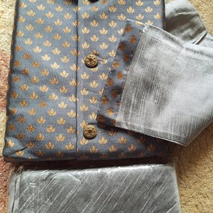May include: A gray kurta with a gold floral pattern and matching pants. The kurta has a mandarin collar and button closure. The pants are plain gray. The label on the kurta says "ELEGANT".