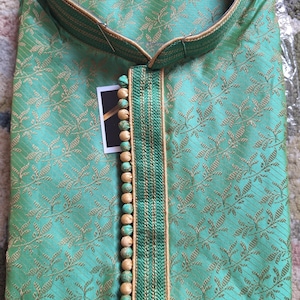 May include: A mint green kurta shirt with a floral pattern and gold trim. The shirt has a mandarin collar and a decorative buttoned placket. The brand name "L.ELEGANT" is visible on the collar.