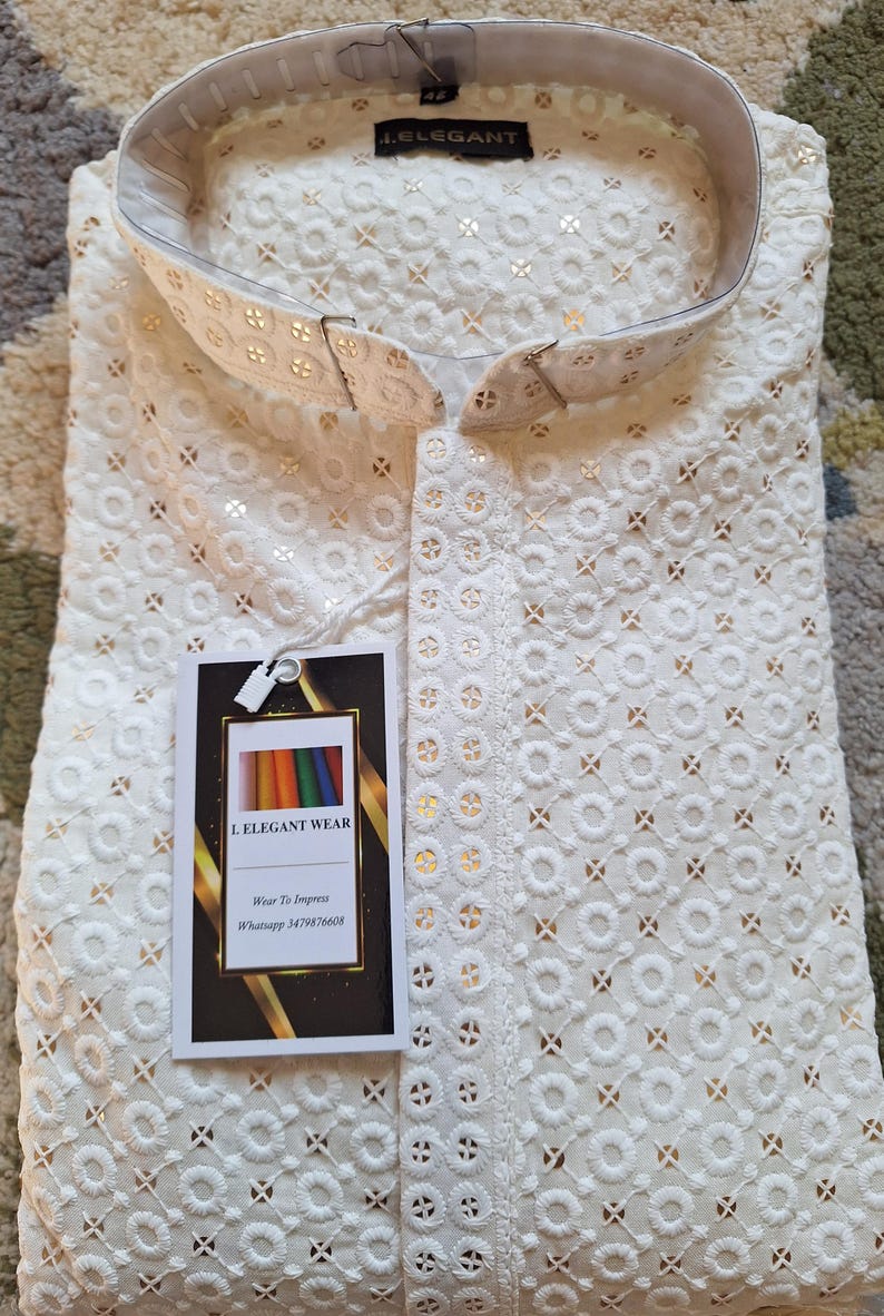 Puede incluir: Camisa blanca de algod&oacute;n con un delicado patr&oacute;n bordado. La camisa tiene un cuello mandar&iacute;n y cierre de botones. La camisa est&aacute; etiquetada con "I. ELEGANT WEAR" y "Wear To Impress".
