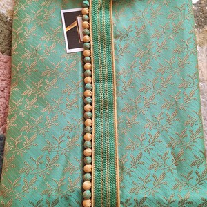 May include: A teal-colored kurta with a floral pattern and a mandarin collar. The neckline is accented with a green and gold trim and wooden beads. The label reads "i.ELEGANT".