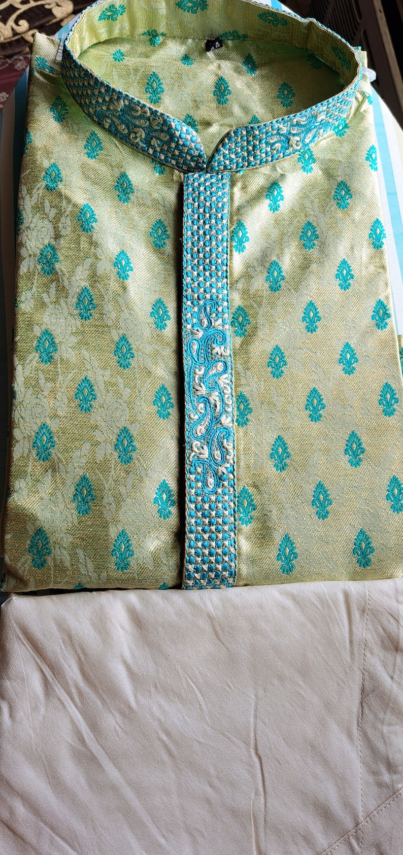 Op de afbeelding: Een lichtgroene kurta met een blauwe en witte geborduurde rand. De kurta heeft een mandarijnkraag en een knoopsluiting.
