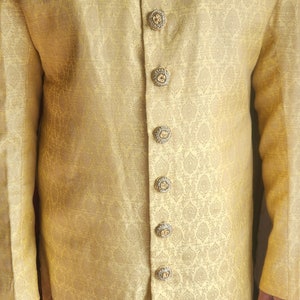 K&ouml;nnte beinhalten: Goldgelbe Jacke mit langen &Auml;rmeln und aufwendigen, sich wiederholenden Mustern. Die Jacke hat dekorative Kn&ouml;pfe und eine kleine Tasche. Kragen und Kn&ouml;pfe sind mit Gold verziert. Es ist ein formelles Kleidungsst&uuml;ck.