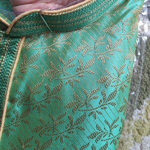 May include: Close-up of a green garment with gold floral embroidery. The collar and trim are a darker green with gold accents. The fabric has a subtle sheen, suggesting a silk or satin material.