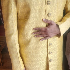 K&ouml;nnte beinhalten: Gelbe Jacke mit Muster, verzierten goldenen Kn&ouml;pfen und einem dekorativen Kragen. Die Jacke hat ein Einstecktuch und ist Teil eines traditionellen Outfits. Das Outfit wird mit einer wei&szlig;en Hose getragen.