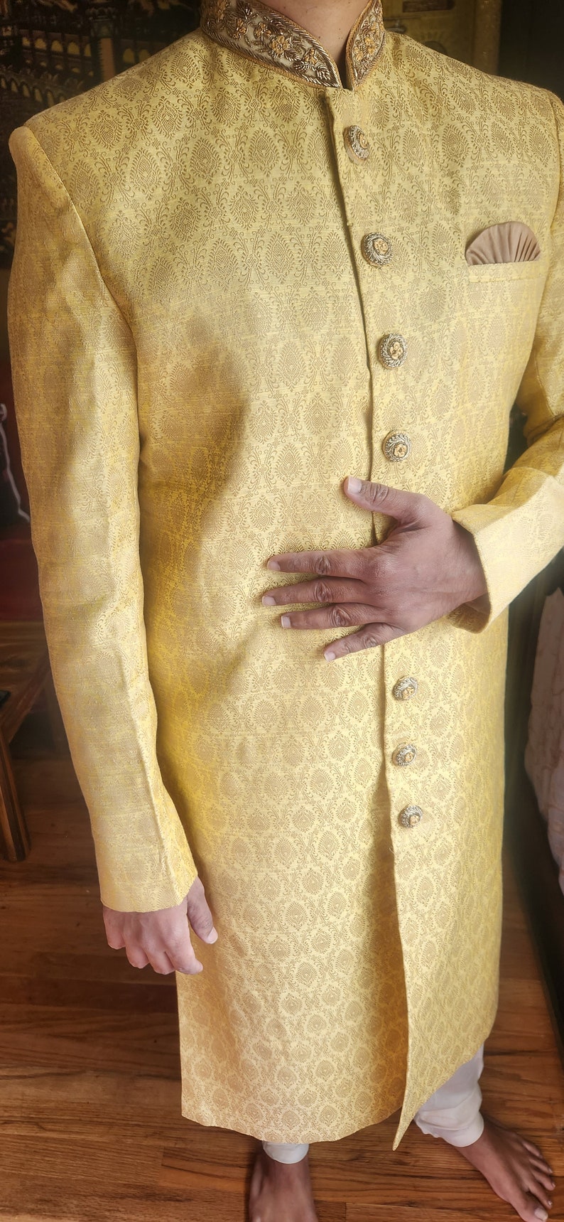 K&ouml;nnte beinhalten: Gelbe Jacke mit Muster, verzierten goldenen Kn&ouml;pfen und einem dekorativen Kragen. Die Jacke hat ein Einstecktuch und ist Teil eines traditionellen Outfits. Das Outfit wird mit einer wei&szlig;en Hose getragen.