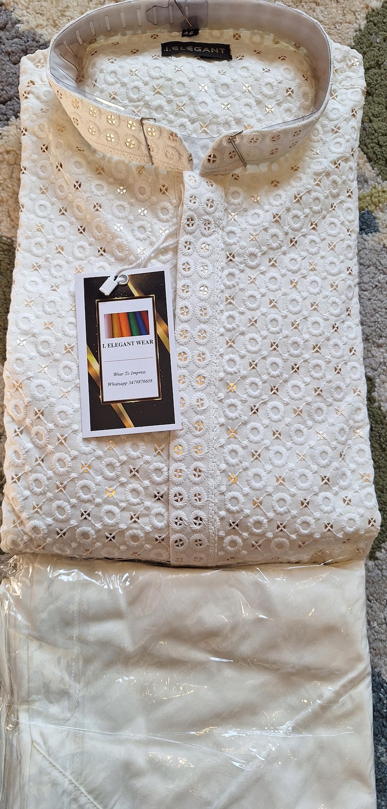 Puede incluir: Kurta blanco bordado con un shalwar blanco. El kurta tiene un cuello mandar&iacute;n y un patr&oacute;n decorativo de peque&ntilde;os c&iacute;rculos y cruces. La etiqueta en el kurta dice "I Elegant Wear" e incluye un n&uacute;mero de tel&eacute;fono: "Whatsapp 3479876608".