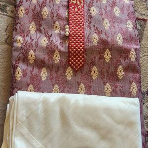 Op de afbeelding: Een maroon kurta met een witte kraag en een rood en gouden geborduurd ontwerp. De kurta wordt gecombineerd met een witte dupatta.