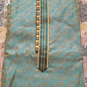 May include: Teal-colored kurta with a gold floral pattern. The neckline is adorned with wooden beads and a decorative trim. The label reads "I.ELEGANT".