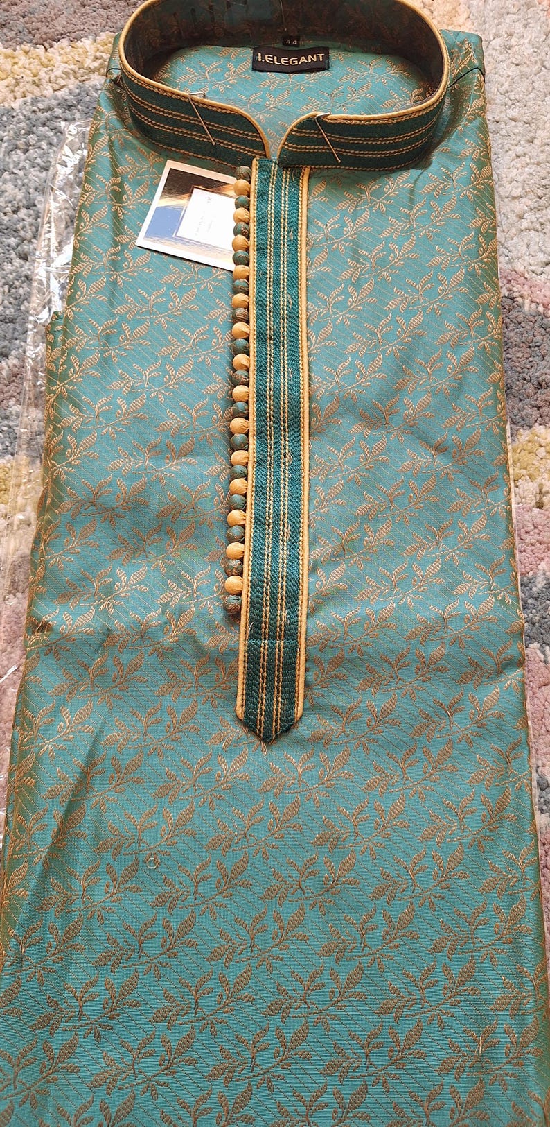 May include: Teal-colored kurta with a gold floral pattern. The neckline is adorned with wooden beads and a decorative trim. The label reads "I.ELEGANT".