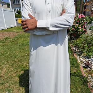 May include: A white long-sleeved shirt with a button-up collar and a pocket on the left chest. The shirt is worn by a person with their arms crossed.