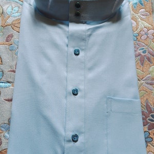 May include: A light blue collared shirt with a button-up closure and a pocket on the right side. The shirt has a label that reads "LELEGANT 54".
