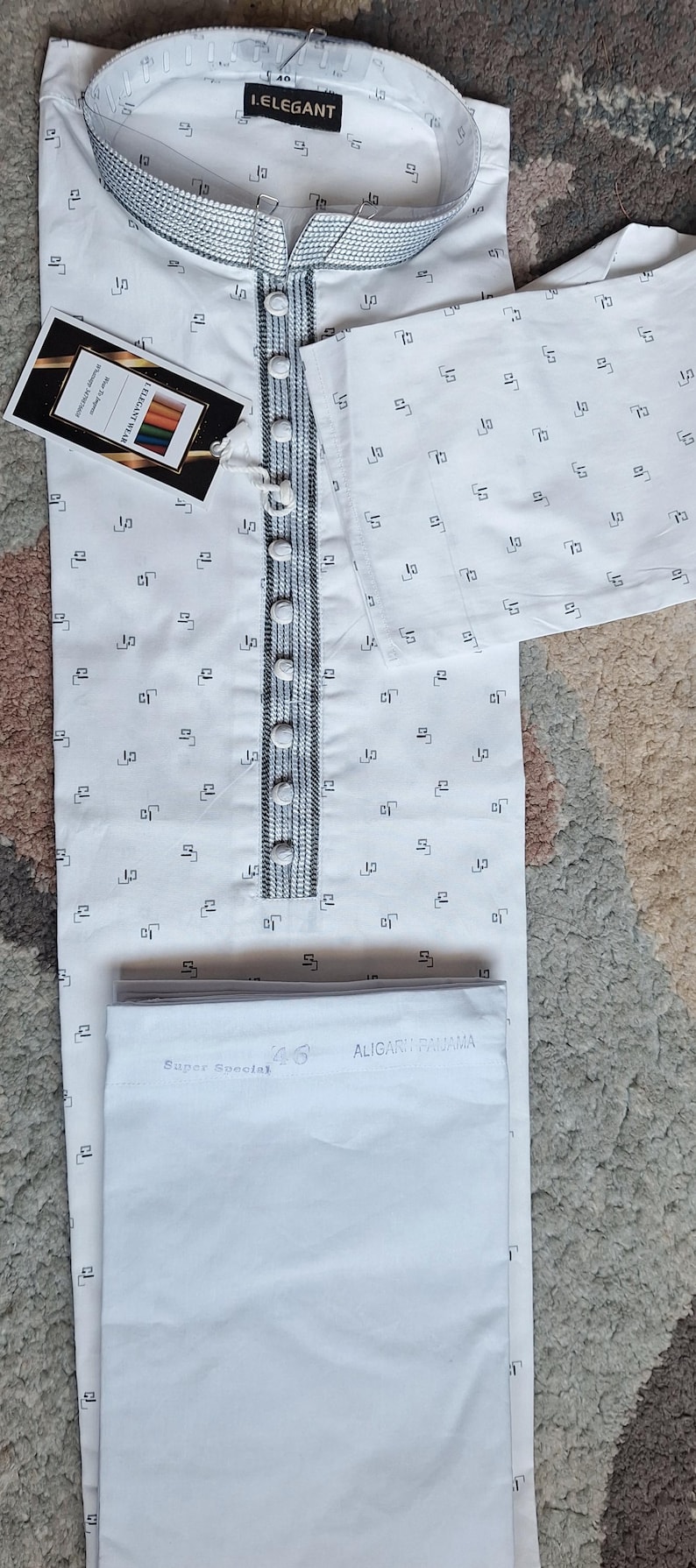 May include: White kurta pajama set with a small black geometric pattern. The kurta features a mandarin collar, button-down front, and decorative trim. The set includes matching pants. A tag reads "I.ELEGANT".