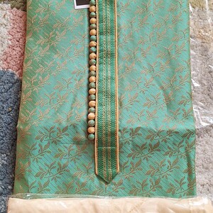May include: A mint green kurta suit with a detailed floral pattern. The neckline is accented with a vertical strip of green and gold trim and wooden beads. The brand name "I.ELEGANT" is visible on the tag.