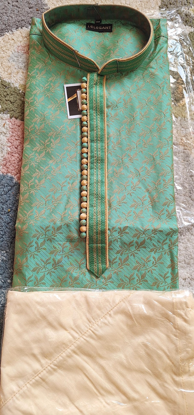 May include: A mint green kurta suit with a detailed floral pattern. The neckline is accented with a vertical strip of green and gold trim and wooden beads. The brand name "I.ELEGANT" is visible on the tag.