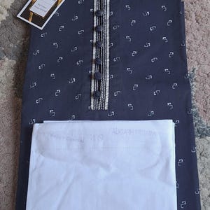 May include: Navy blue kurta pajama set. The kurta features a small white geometric pattern, a button-down front, and a decorative collar. The set includes a matching white pajama. A tag with the brand name is attached.