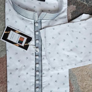 May include: White kurta pajama set with a small black geometric pattern. The kurta features a mandarin collar and a button-down front with decorative trim. A tag with the text "I.ELEGANT" is attached.