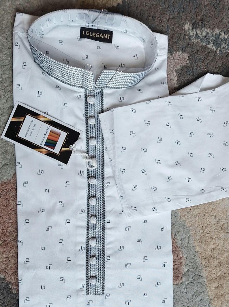 May include: White kurta pajama set with a small black geometric pattern. The kurta features a mandarin collar and a button-down front with decorative trim. A tag with the text "I.ELEGANT" is attached.