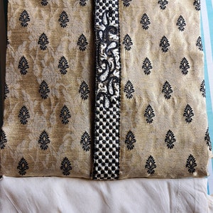 Op de afbeelding: Een gouden kurta met zwarte borduursels en een witte kraag. De kurta is gevouwen en gelegd op een witte stof.
